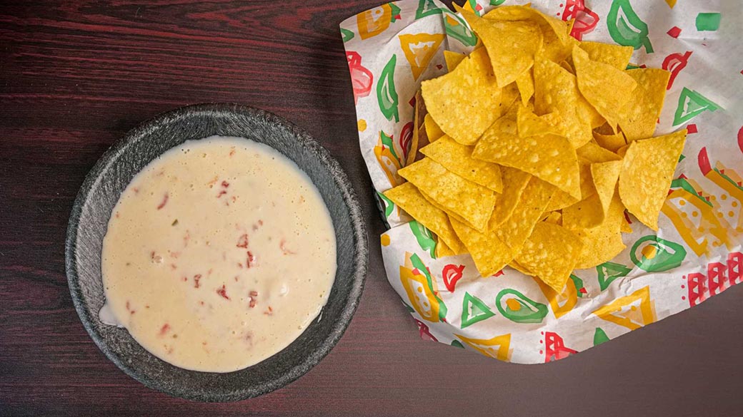 A bowl of freshly made queso dip, served with warm, crispy tortilla chips.