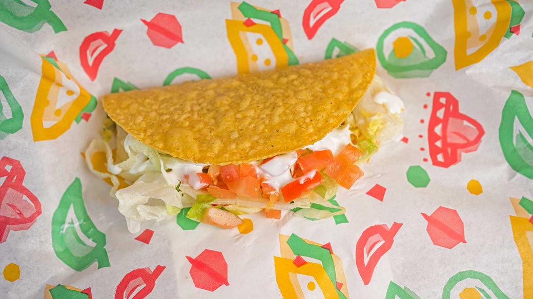 A crispy taco shell filled with seasoned meat, shredded lettuce, diced tomatoes, and a drizzle of creamy sauce.